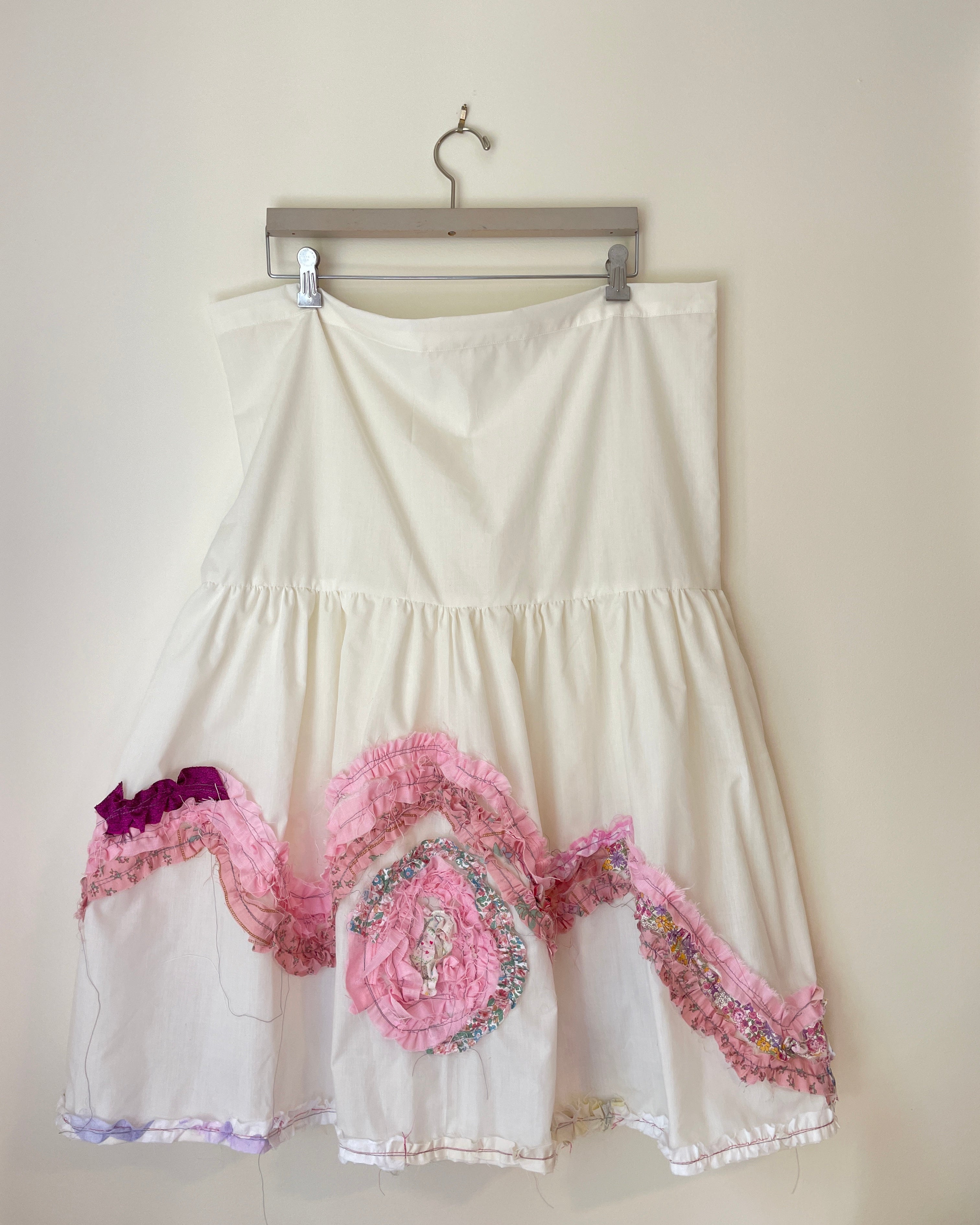 White dress with pink floral embroidery on a hanger against a white background