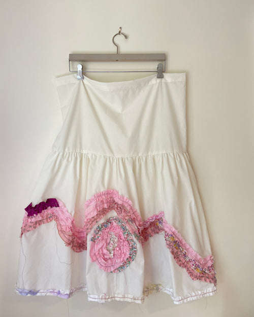 White dress with pink floral embroidery on a hanger against a white background