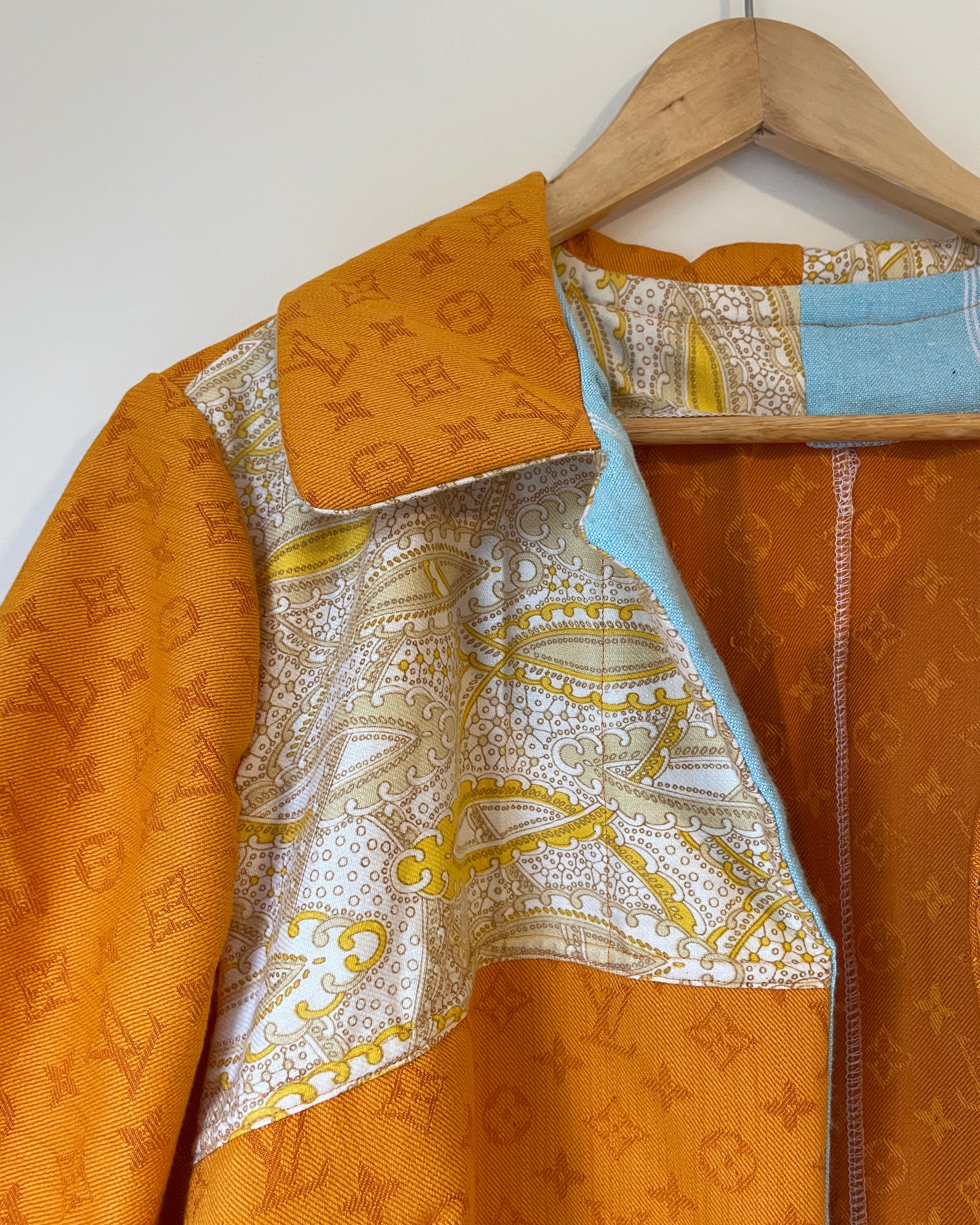 Orange jacket with patterned lining on a wooden hanger against a white wall