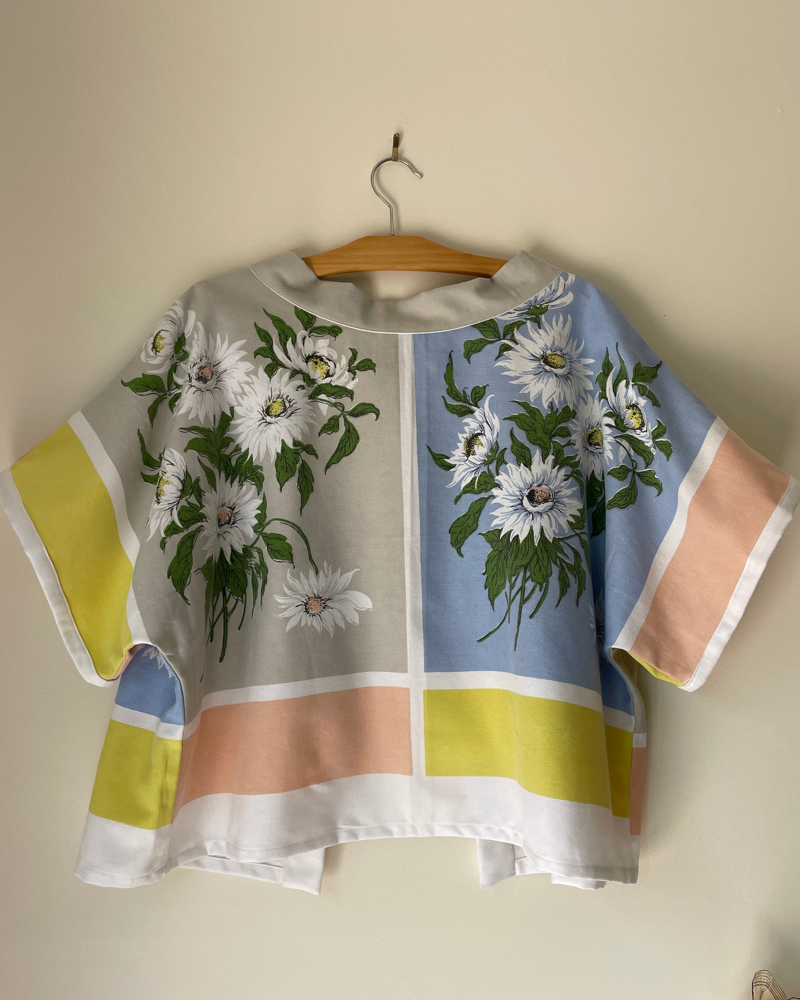 Colorful blouse with floral design on a wooden hanger against a beige wall