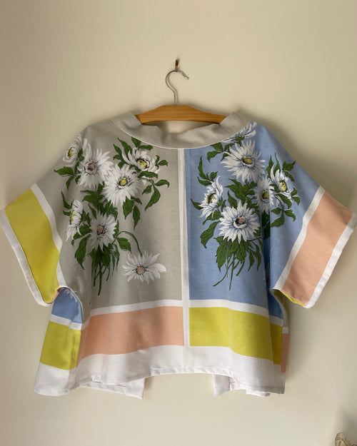 Colorful blouse with floral design on a wooden hanger against a beige wall
