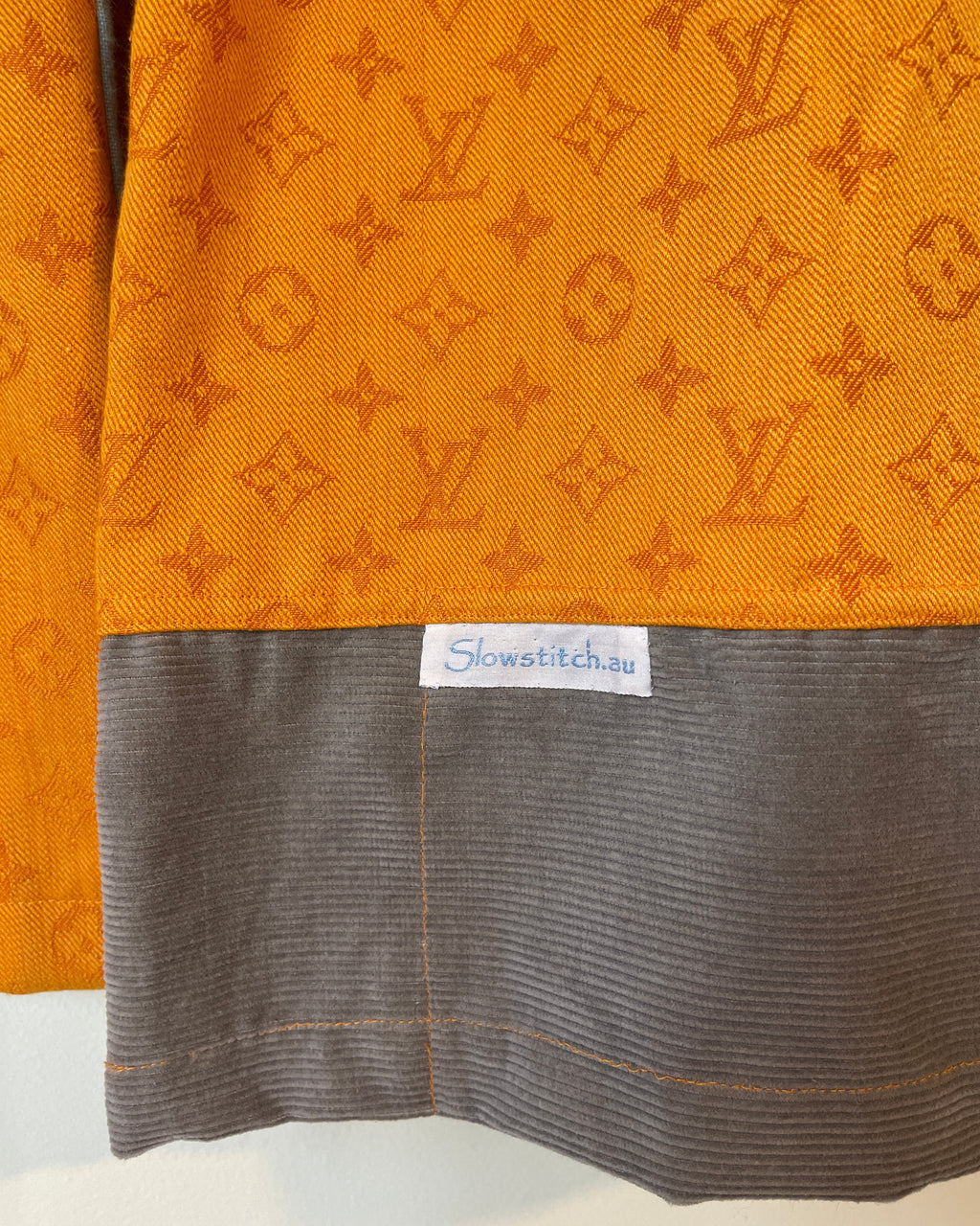 Close-up of orange fabric with a pattern and a gray fabric with a brand label.