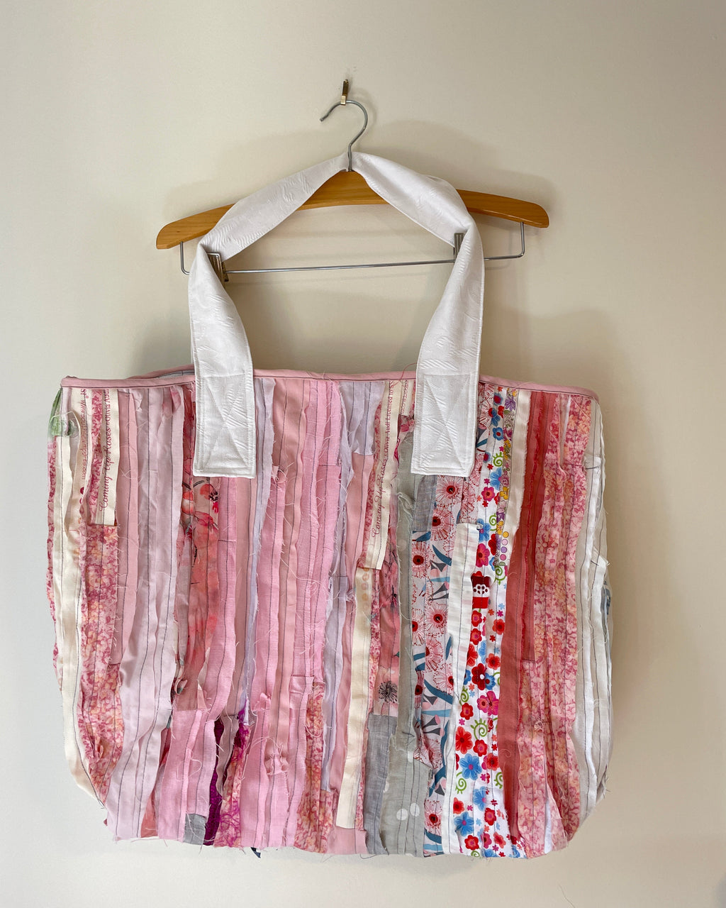 Tote bag on a wooden hanger against a beige wall.
