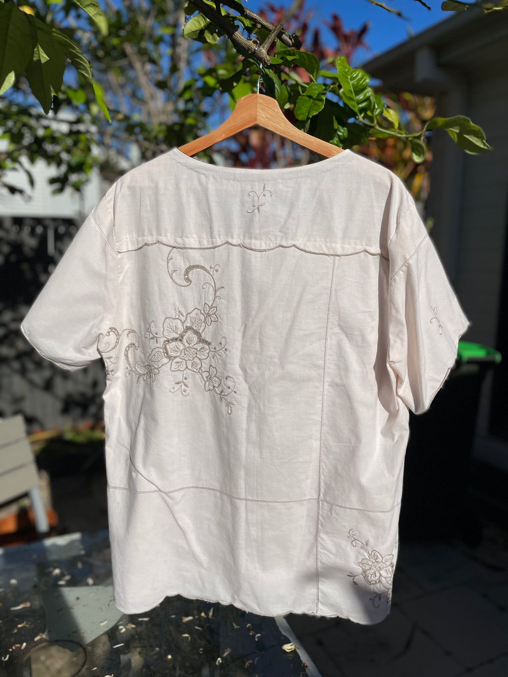 White blouse with floral embroidery on a wooden hanger against a blurred outdoor background