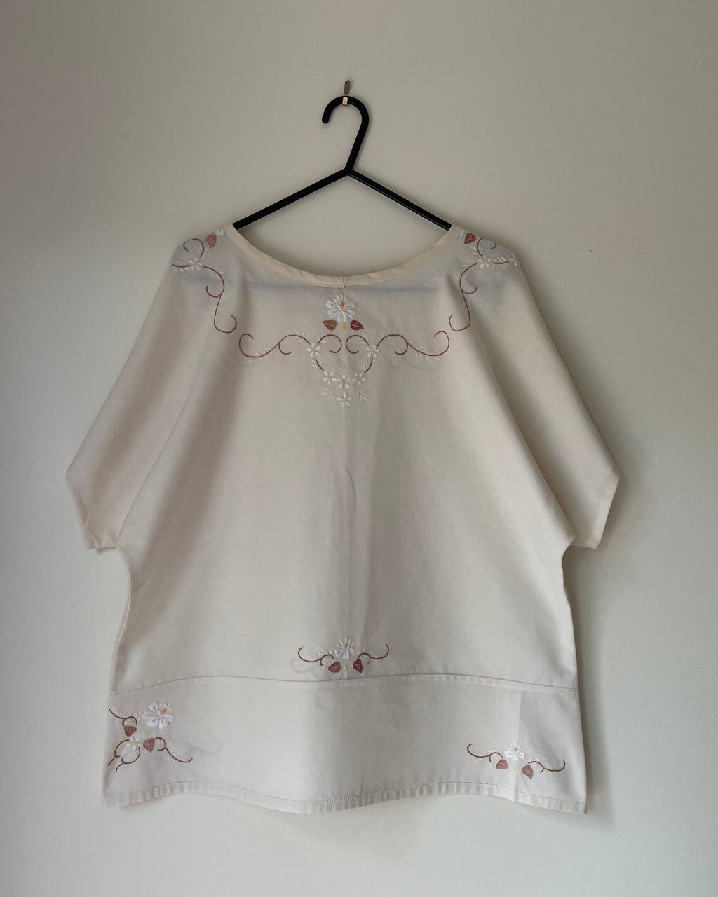 White blouse with embroidery on a hanger against a plain background