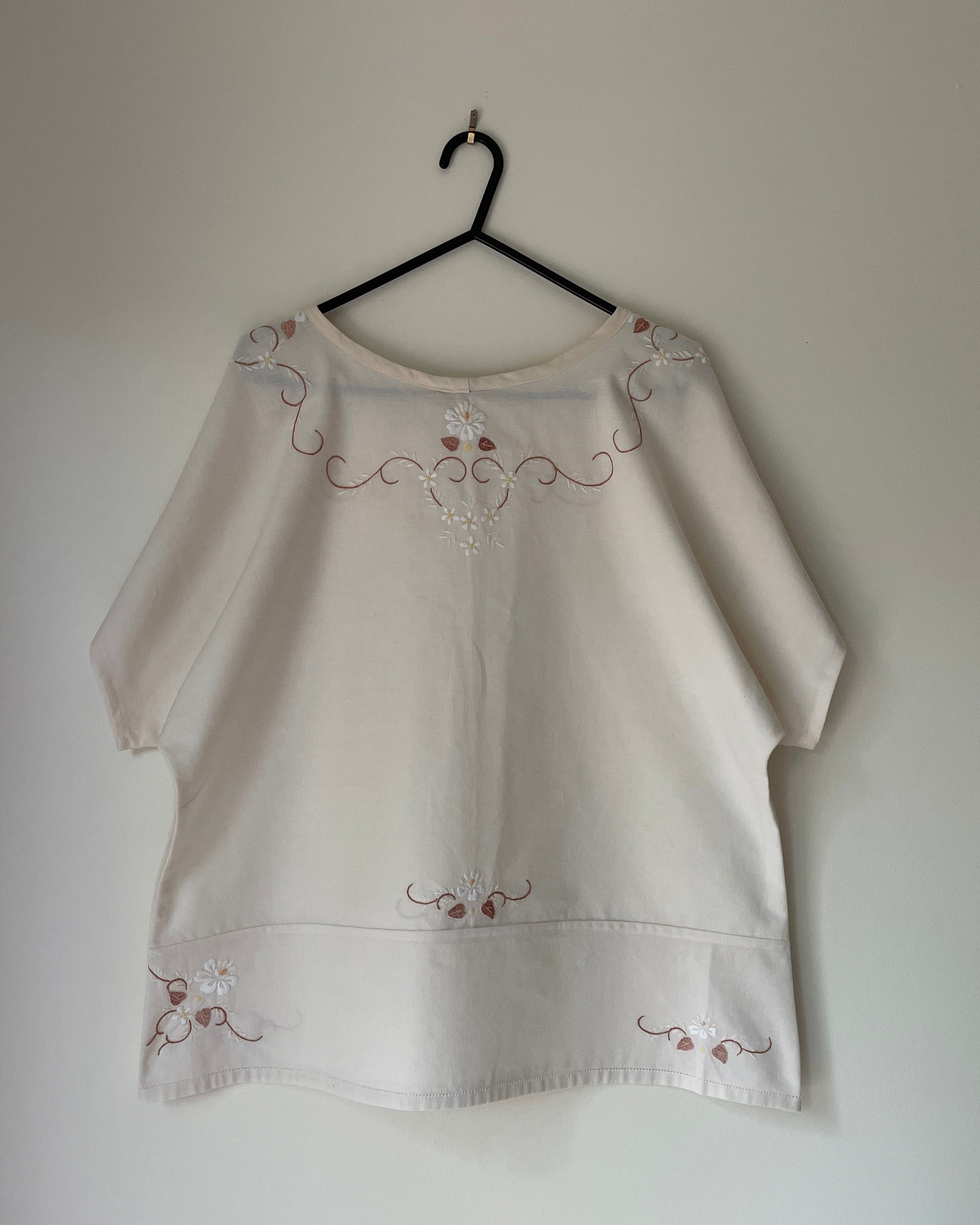 White blouse with embroidery on a hanger against a plain background