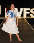Model on a runway wearing a colourful top and white skirt with 'MVFS' sign in the background.