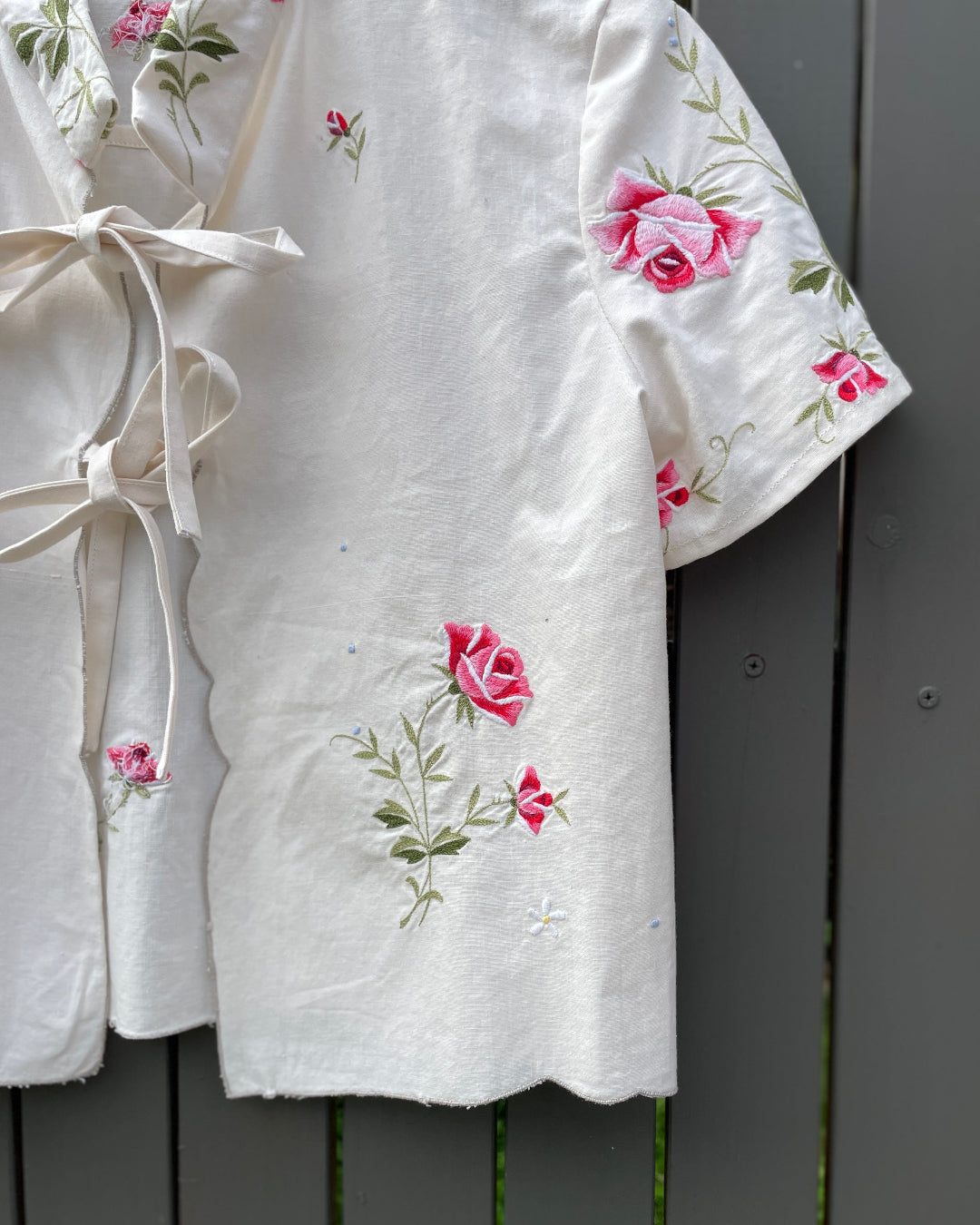 White robe with pink floral embroidery on a dark wooden surface