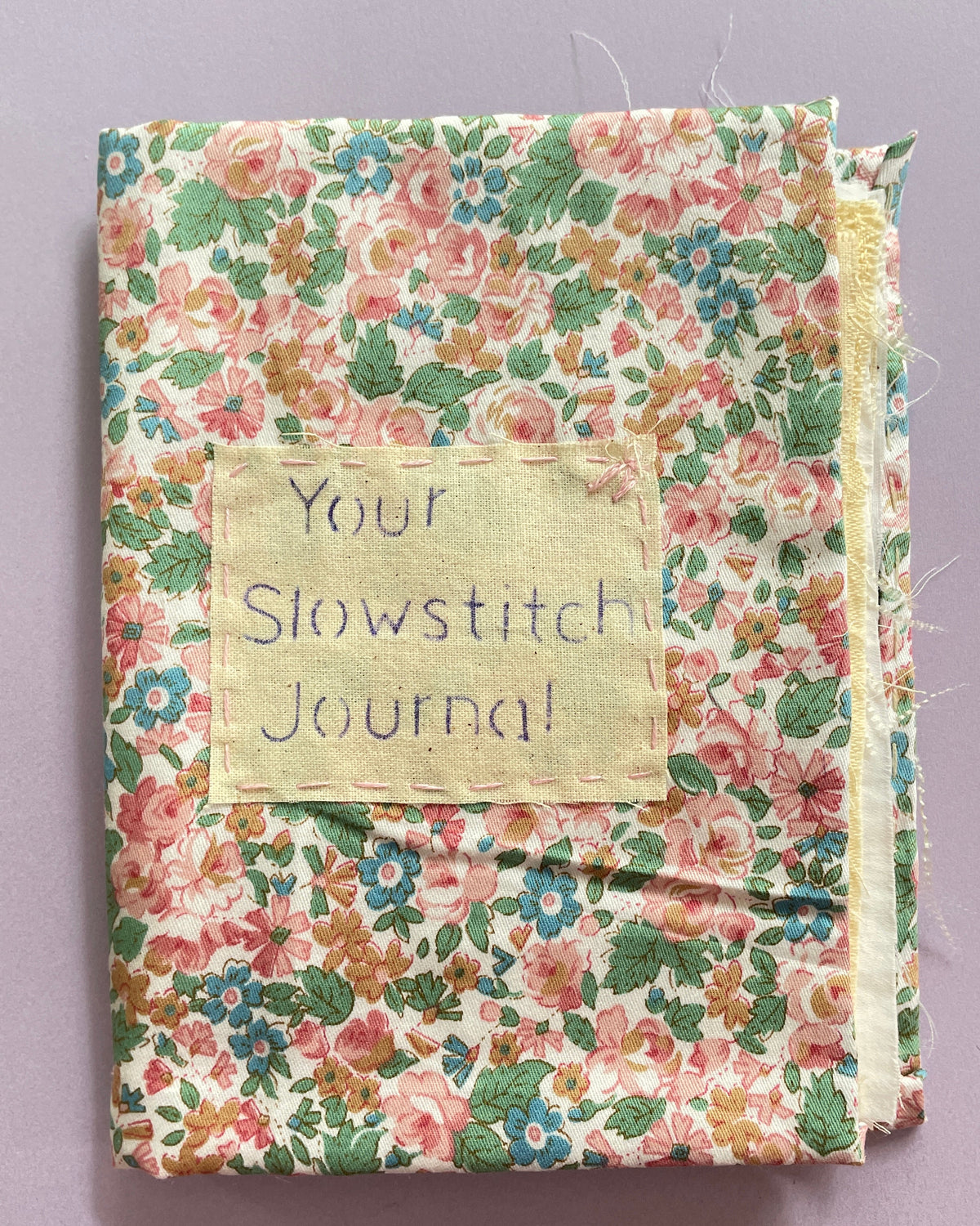 Floral fabric journal with 'Your Slow Stitch Journal' label on a purple background