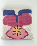 A square woven throw pillow featuring a stylized pansy design in pink, blue, yellow, and black on a cream mesh background.