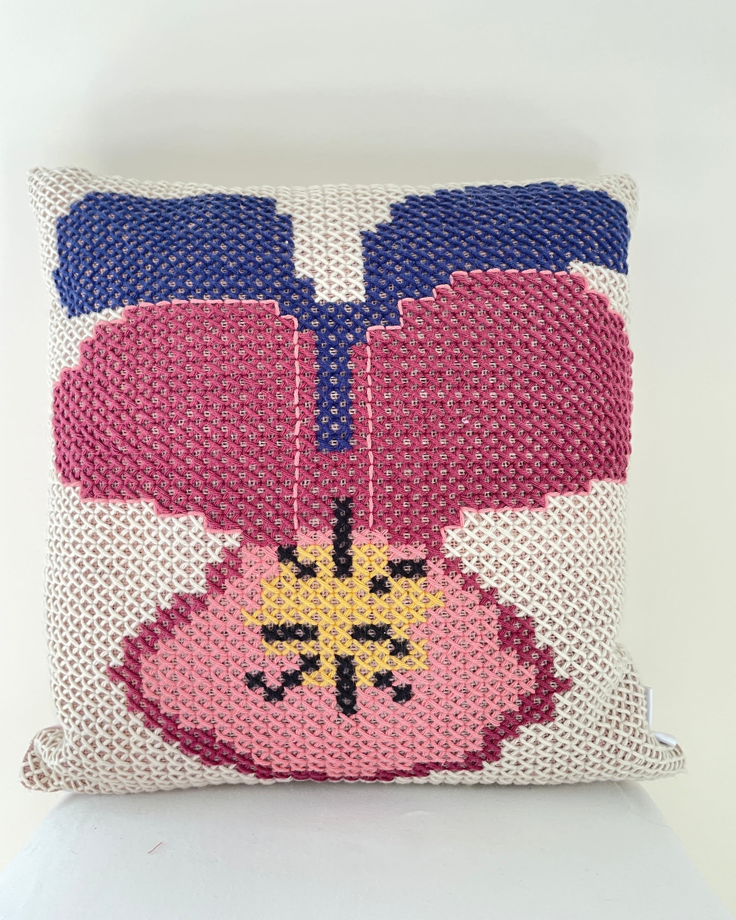 A square woven throw pillow featuring a stylized pansy design in pink, blue, yellow, and black on a cream mesh background.